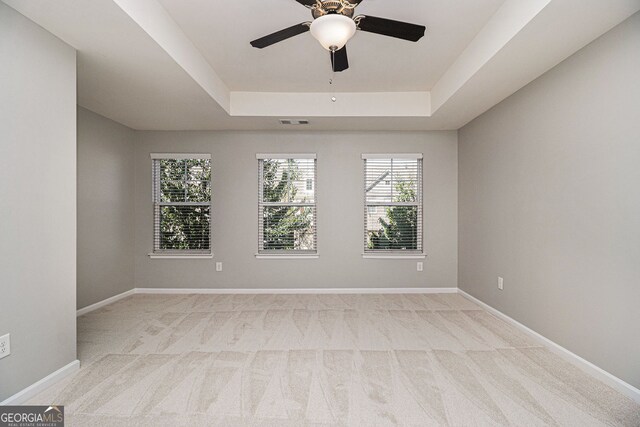 spare room with ceiling fan, a raised ceiling, baseboards, and light carpet