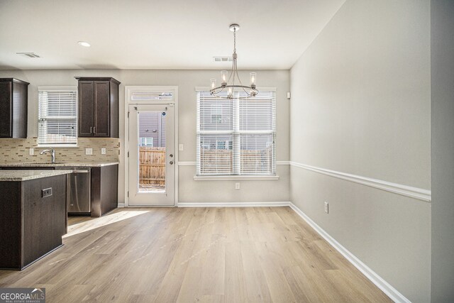 kitchen with stainless steel dishwasher, light wood-style flooring, visible vents, decorative columns, and ceiling fan with notable chandelier