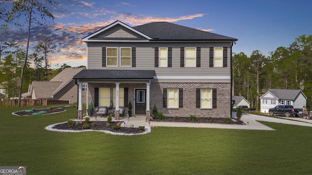 view of front of home featuring covered porch, brick siding, a yard, and roof with shingles