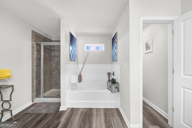 bathroom featuring a garden tub, a stall shower, wood finished floors, and baseboards