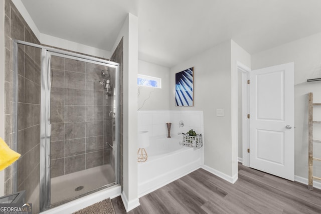bathroom with a bath, a shower stall, wood finished floors, and baseboards