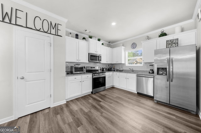 kitchen with wood finished floors, a toaster, appliances with stainless steel finishes, white cabinets, and crown molding