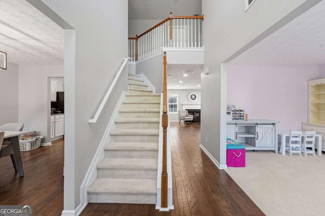 stairway featuring a towering ceiling, baseboards, a textured ceiling, visible vents, and wood finished floors