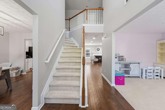 stairway featuring hardwood / wood-style floors, a high ceiling, and baseboards