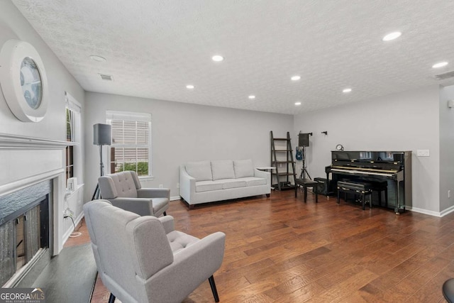 living room with a textured ceiling, wood finished floors, a fireplace, and visible vents