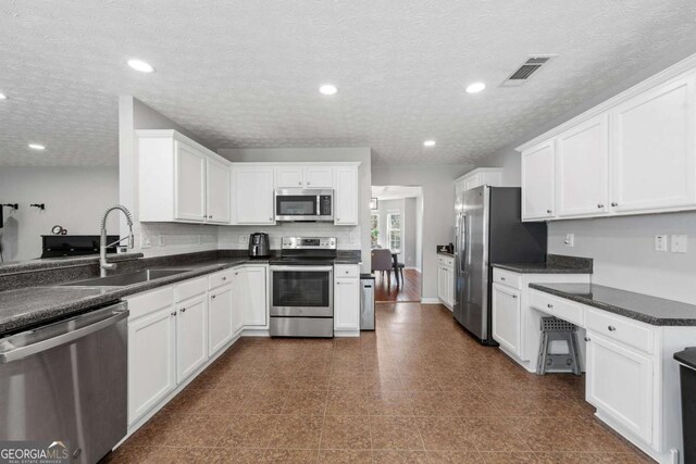 kitchen featuring white cabinetry, dark countertops, visible vents, appliances with stainless steel finishes, and a sink