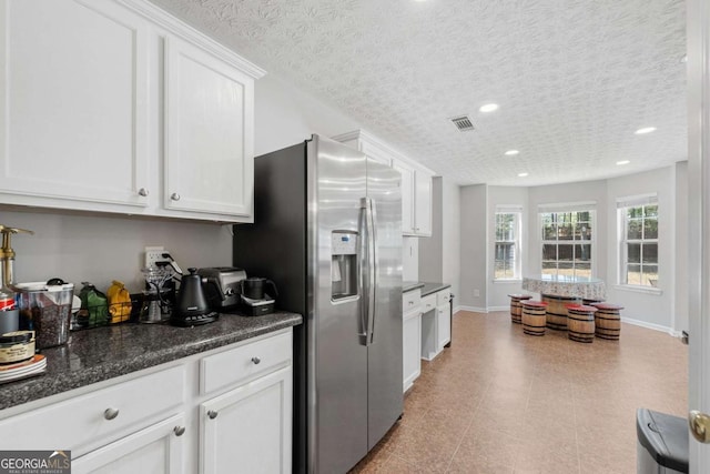 kitchen with a textured ceiling, visible vents, white cabinets, stainless steel refrigerator with ice dispenser, and baseboards