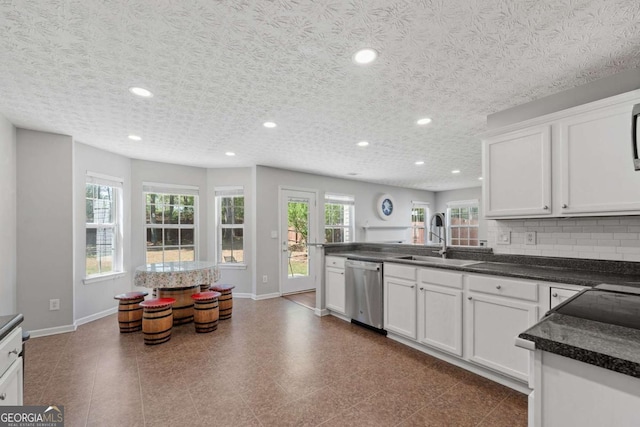 kitchen featuring tasteful backsplash, a sink, dark countertops, a peninsula, and stainless steel dishwasher