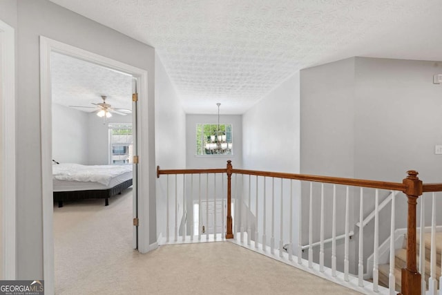 corridor featuring a textured ceiling, an upstairs landing, a notable chandelier, and carpet
