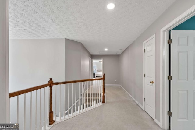 hall featuring baseboards, light carpet, an upstairs landing, a textured ceiling, and attic access