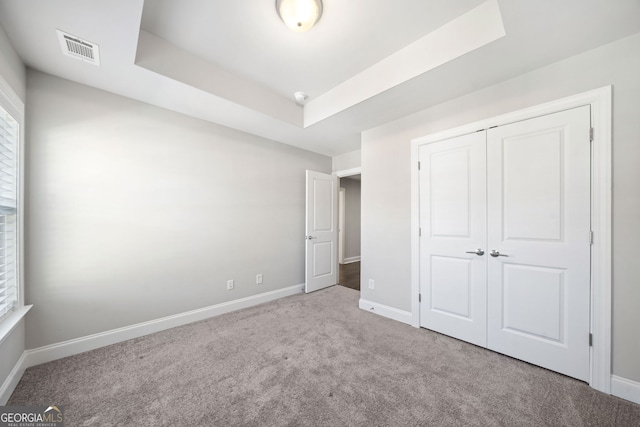unfurnished bedroom with carpet flooring, visible vents, a tray ceiling, and baseboards