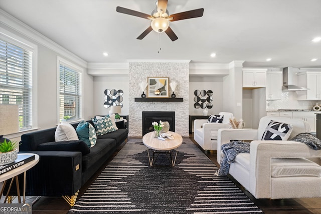 living room with a ceiling fan, ornamental molding, a stone fireplace, and recessed lighting