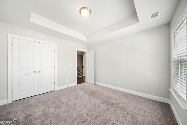unfurnished bedroom featuring visible vents, baseboards, a tray ceiling, and carpet