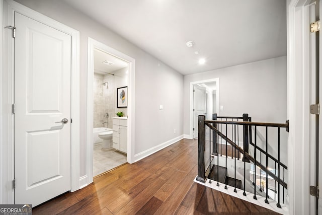 hallway featuring wood finished floors, baseboards, and an upstairs landing