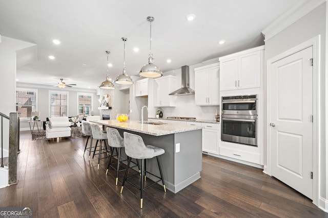 kitchen with dark wood finished floors, appliances with stainless steel finishes, wall chimney exhaust hood, and a ceiling fan