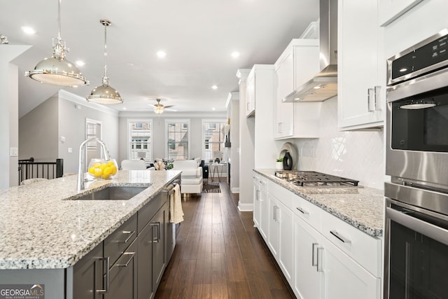 kitchen featuring wall chimney exhaust hood, a sink, ceiling fan, white cabinetry, and stainless steel appliances
