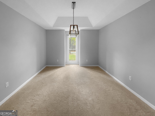 carpeted spare room featuring a tray ceiling and baseboards