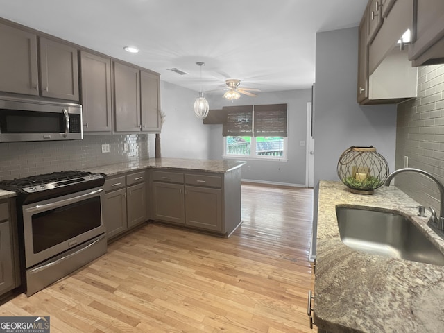 kitchen with a peninsula, appliances with stainless steel finishes, a sink, and light wood-style floors