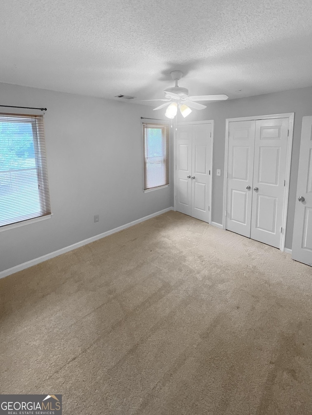 unfurnished bedroom with baseboards, two closets, a ceiling fan, a textured ceiling, and carpet flooring