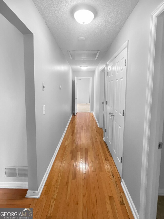 hall featuring light wood-style floors, visible vents, a textured ceiling, and baseboards