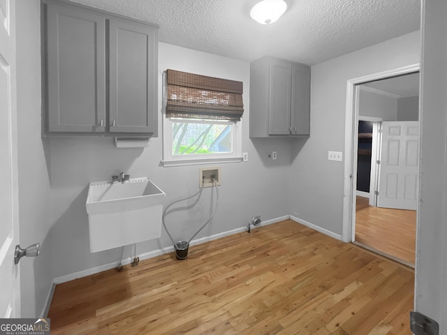 laundry room with baseboards, a textured ceiling, hookup for a washing machine, cabinet space, and light wood finished floors