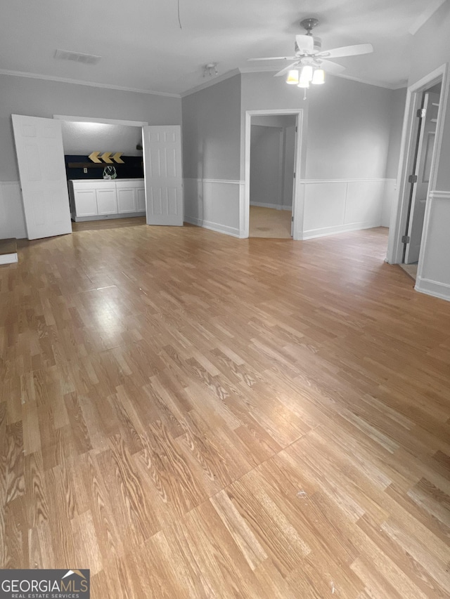 unfurnished living room featuring crown molding, light wood finished floors, a ceiling fan, and wainscoting