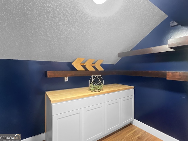 bathroom featuring a textured ceiling, wood finished floors, baseboards, and vaulted ceiling