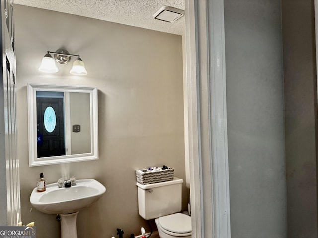half bath with visible vents, a textured ceiling, a sink, and toilet