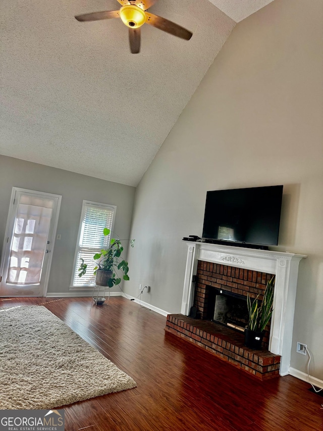 living area featuring baseboards, a brick fireplace, a ceiling fan, a textured ceiling, and wood finished floors