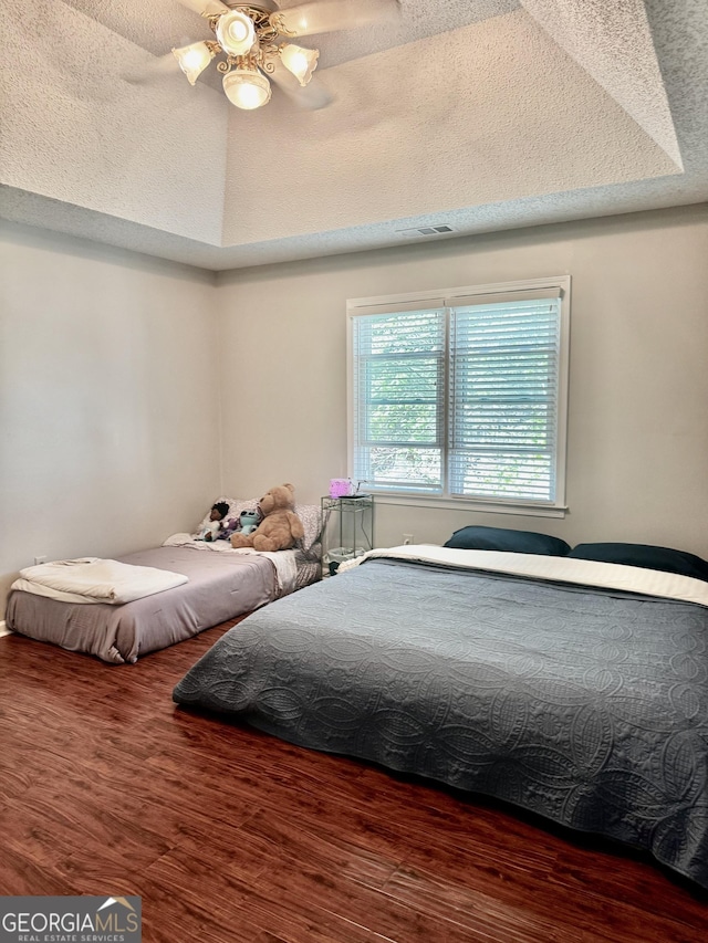 bedroom featuring a tray ceiling, wood finished floors, a ceiling fan, and visible vents