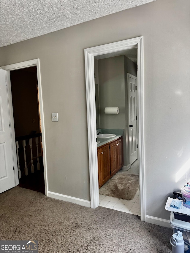 bedroom with light carpet, ensuite bath, baseboards, and a textured ceiling