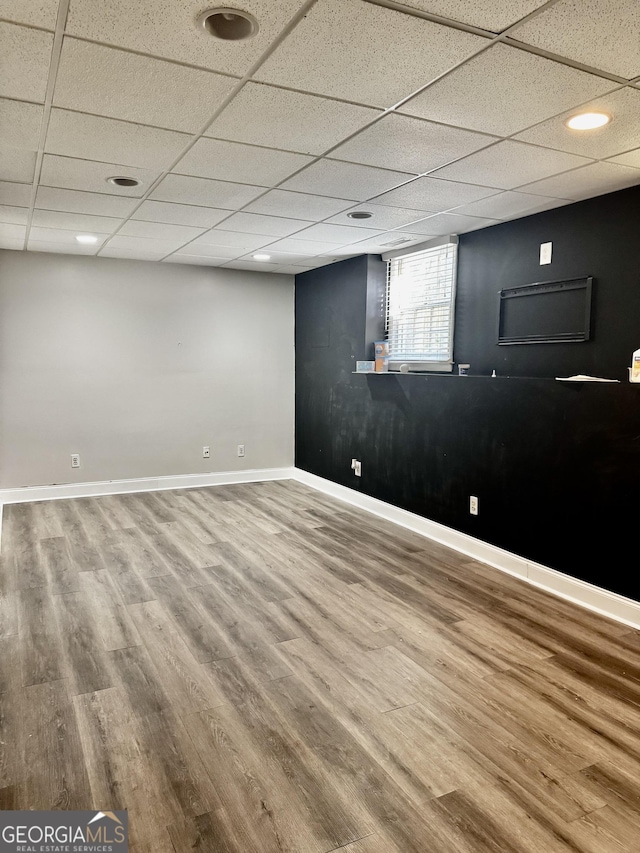 below grade area with baseboards, a paneled ceiling, and wood finished floors