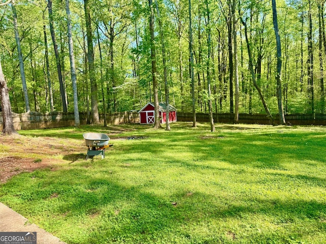 view of yard with a forest view, a shed, a fenced backyard, and an outdoor structure
