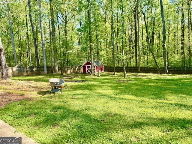 view of yard with an outbuilding, a fenced backyard, a forest view, and a storage unit