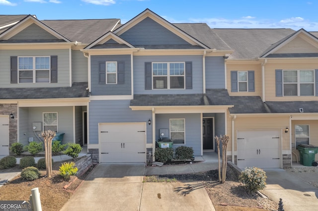 multi unit property featuring an attached garage, a shingled roof, and concrete driveway