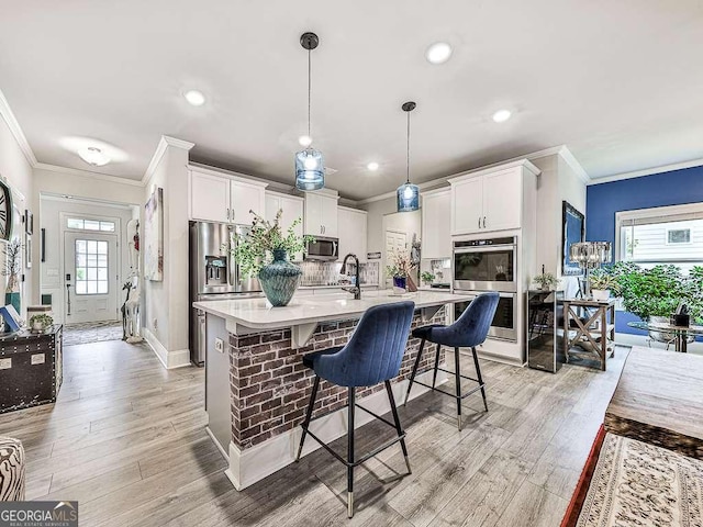 kitchen featuring stainless steel appliances, an island with sink, white cabinets, and crown molding