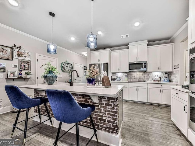 kitchen featuring visible vents, white cabinets, appliances with stainless steel finishes, a kitchen breakfast bar, and crown molding