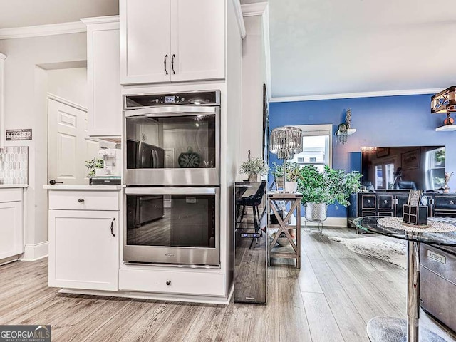 kitchen with crown molding, white cabinets, light wood finished floors, and stainless steel double oven