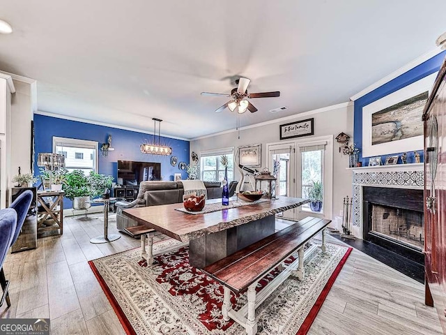 living area featuring light wood-type flooring, ornamental molding, a ceiling fan, visible vents, and a tile fireplace