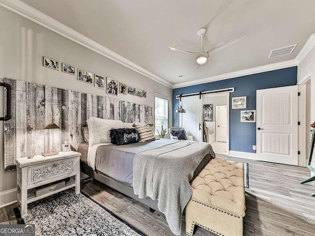 bedroom featuring a barn door, visible vents, ornamental molding, and wood finished floors