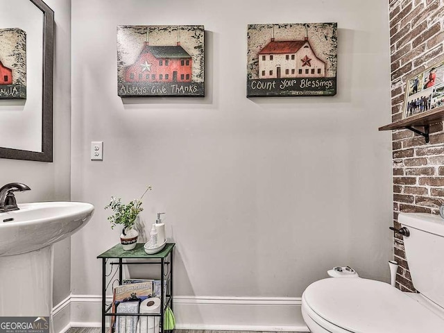 half bath featuring toilet, brick wall, a sink, and baseboards
