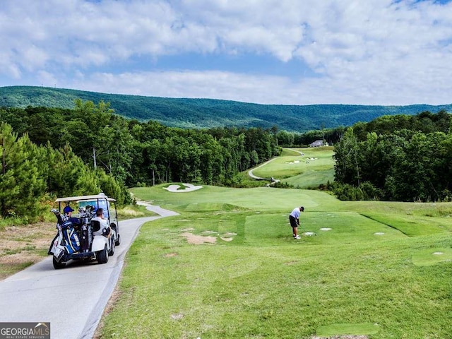 surrounding community featuring a wooded view, golf course view, a lawn, and driveway