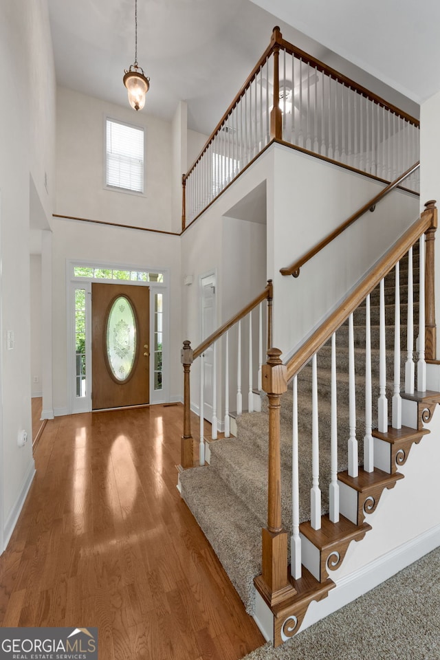 entryway with a towering ceiling, stairs, wood finished floors, and baseboards