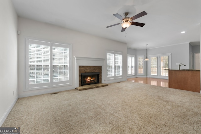 unfurnished living room featuring a ceiling fan, visible vents, carpet, and a warm lit fireplace