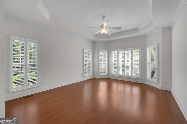 empty room featuring wood finished floors, ornamental molding, ceiling fan, visible vents, and a raised ceiling