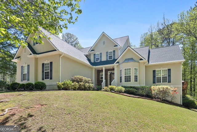 view of front facade featuring a front lawn, a shingled roof, and stucco siding