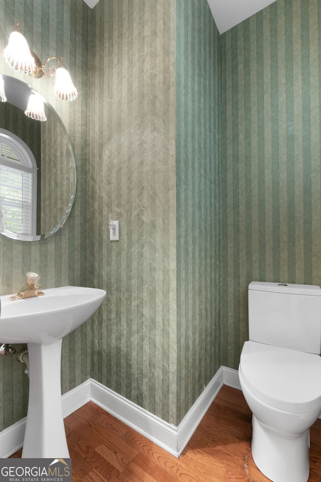 half bathroom with a sink, wood finished floors, toilet, and baseboards