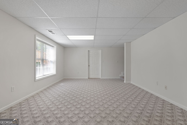 carpeted empty room with baseboards, visible vents, and a drop ceiling