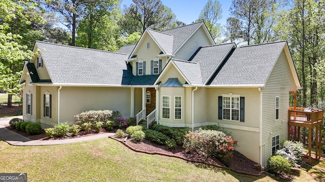 view of front of home featuring a front yard, a wooden deck, a shingled roof, and stucco siding