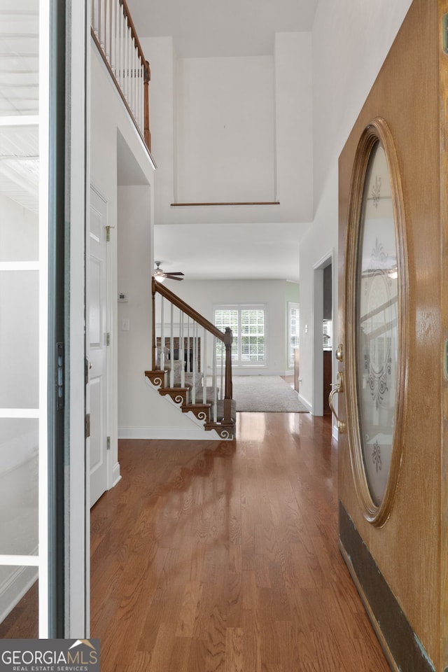 entryway featuring stairway, ceiling fan, baseboards, a towering ceiling, and wood finished floors